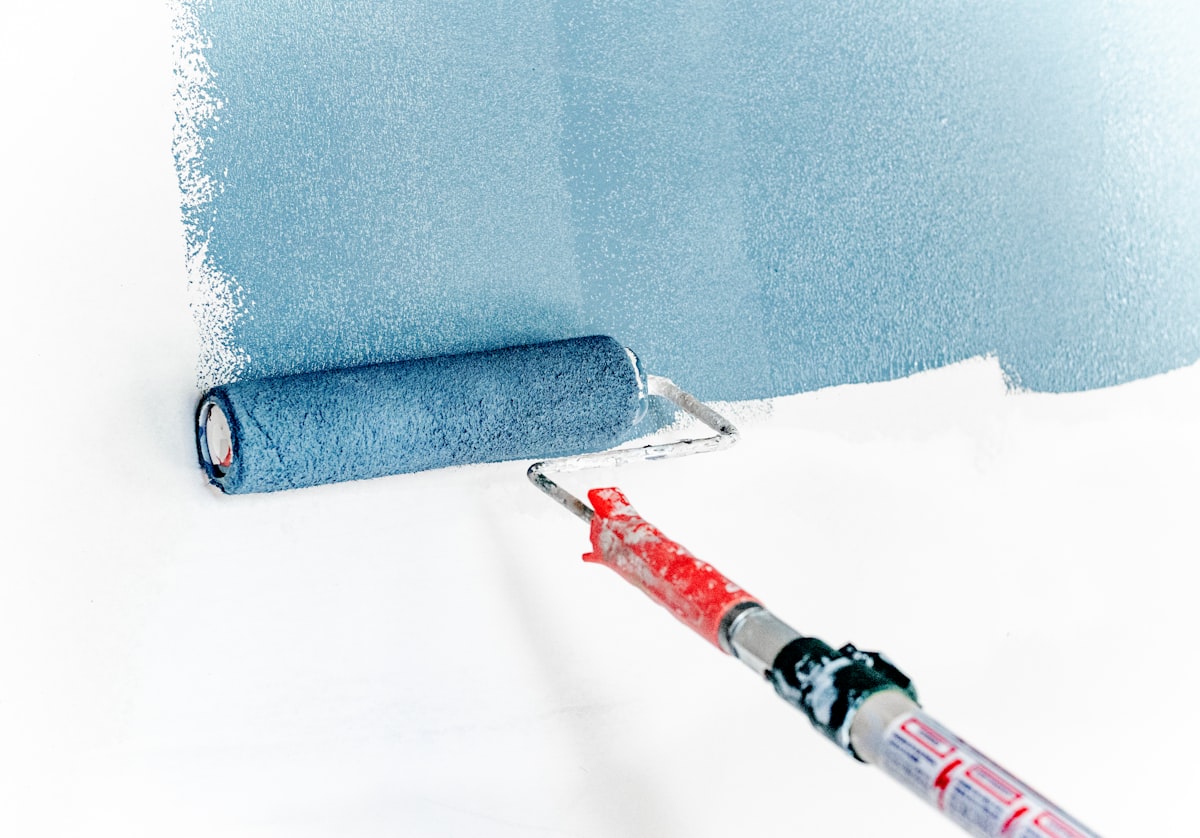 Paint roller applying a fresh coat of blue-gray paint to a wall